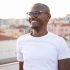 African American man smiling in white shirt with cityscape backdrop.